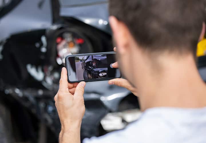 Man looking at iPhone photographing damage to car.
